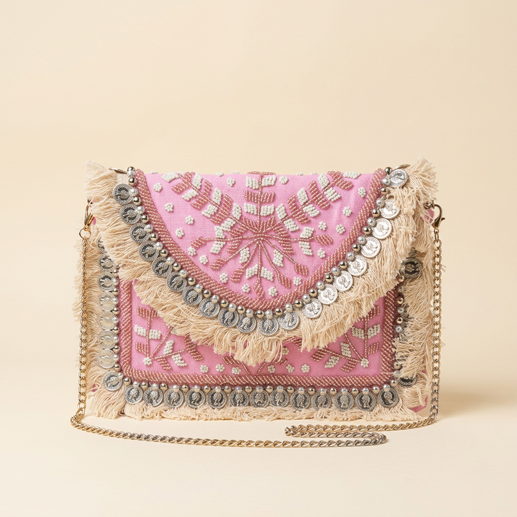 Pink beaded boho clutch with coin trim and cotton fringe on a cream studio background