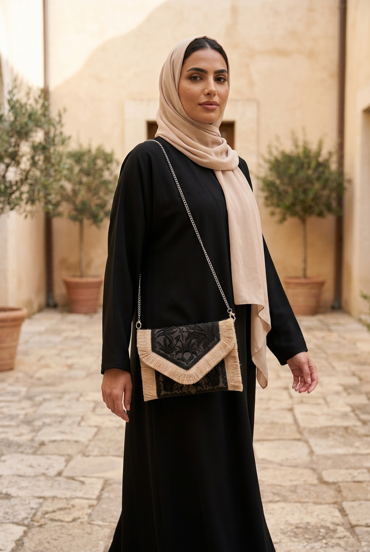 Black and beige floral sequin fringe clutch on a silver chain with a black abaya and beige shayla in a stone courtyard