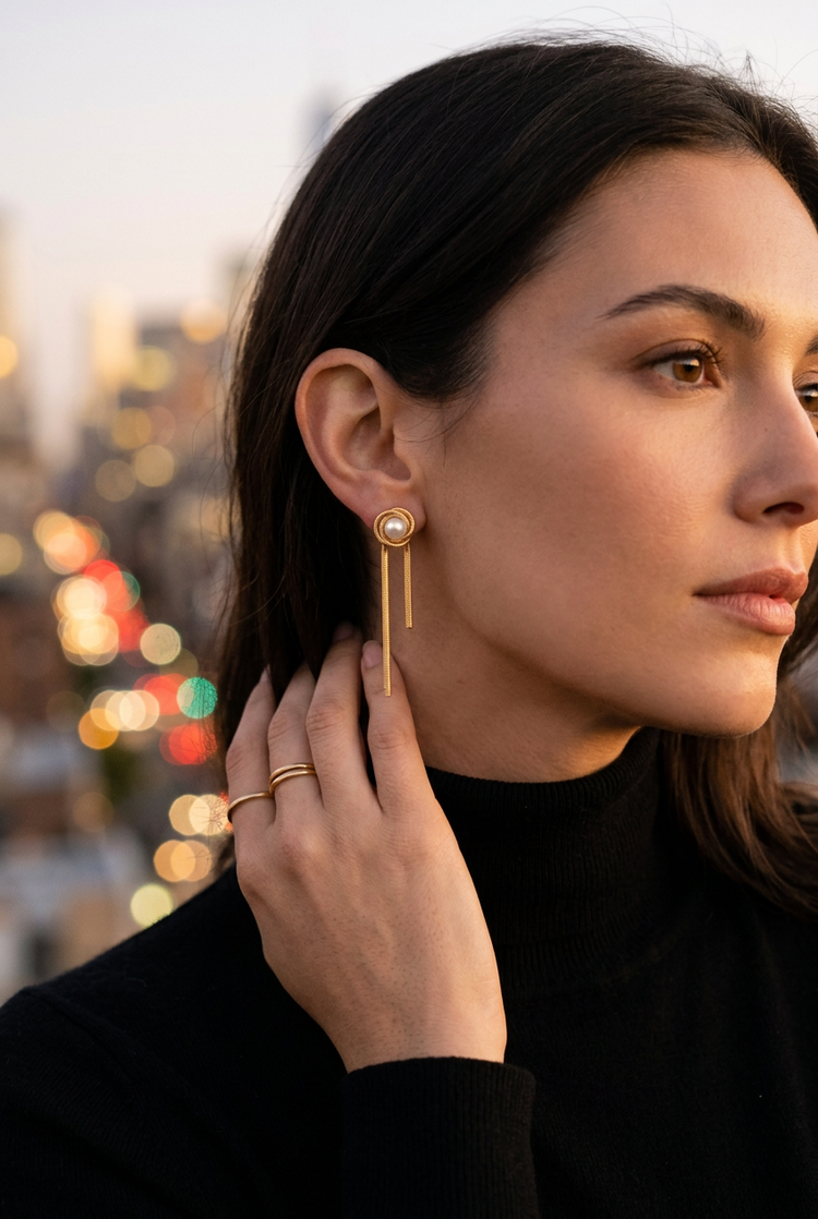 Pearl knot gold chain earrings worn on an evening rooftop
