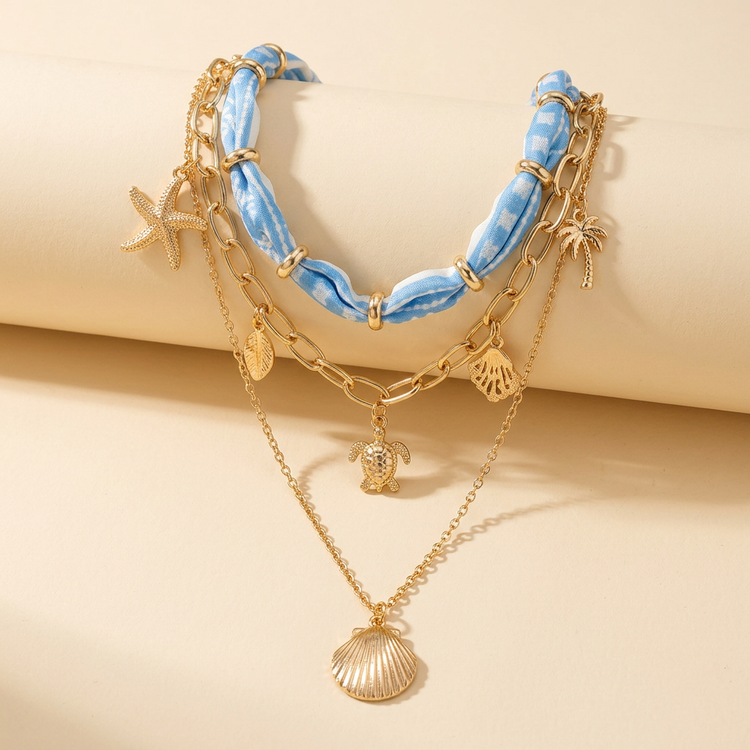 Blue scarf and gold seashell layered necklace on cream studio background