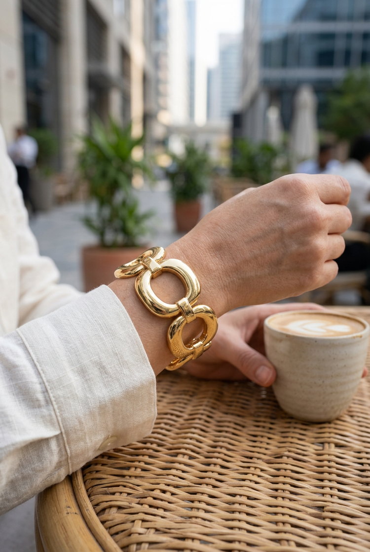 Sculpted oval-link gold bracelet worn with ivory linen at a café