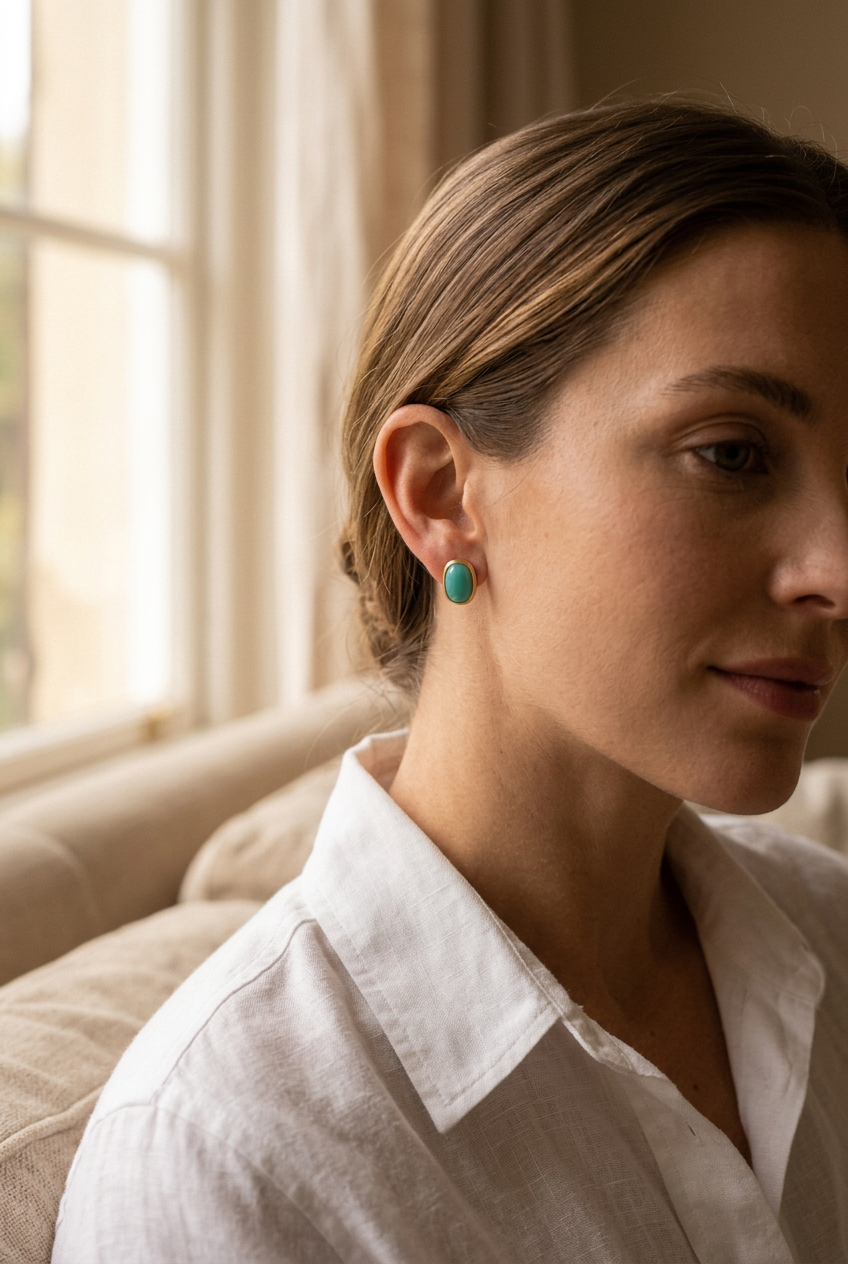 Aqua oval gold studs worn with a white shirt by a window