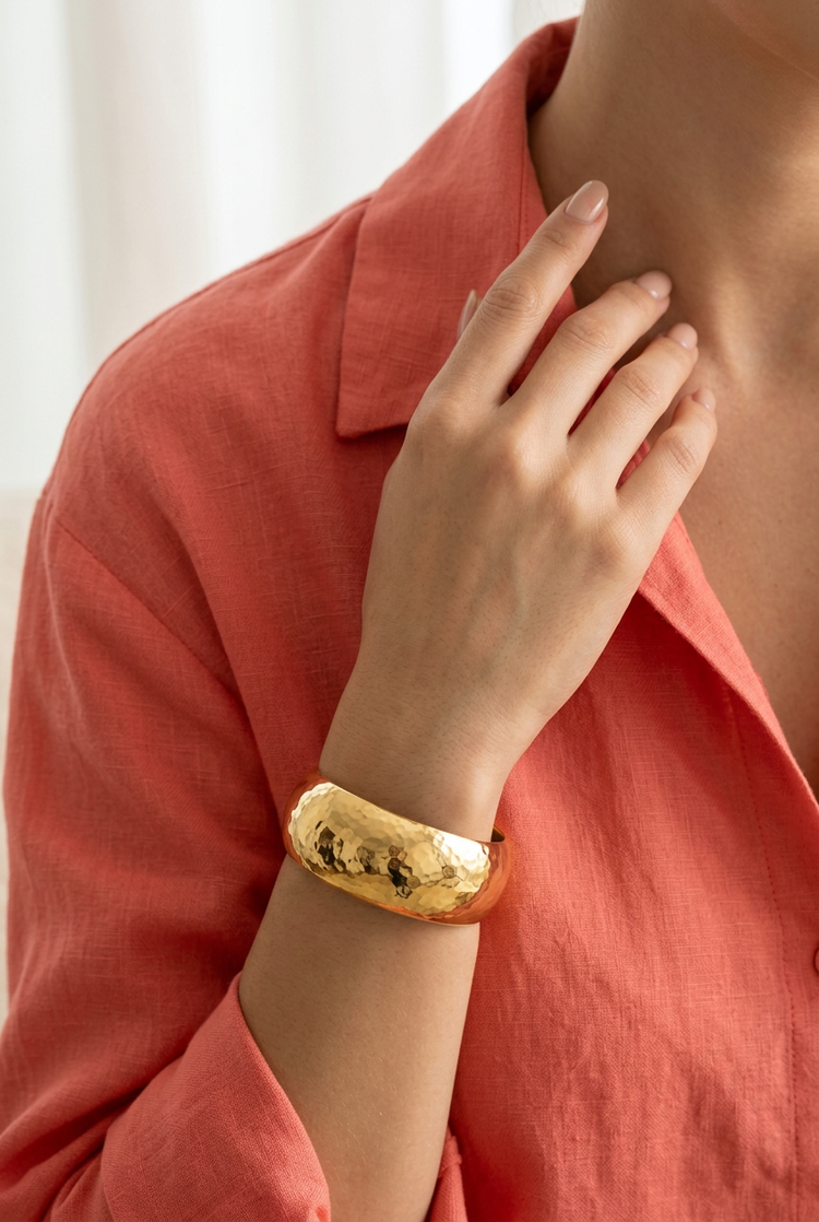 Woman in a coral linen shirt wearing a wide hammered gold bangle