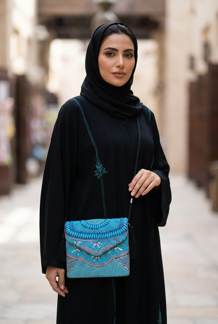 Turquoise beaded crossbody bag worn with a black turquoise-embroidered abaya in a souk arcade