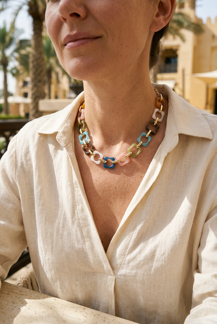 Small short multicolour square-link necklace worn near the collarbone with cream linen