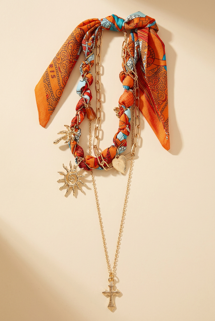 Orange paisley scarf and layered gold charm necklace on a cream studio background