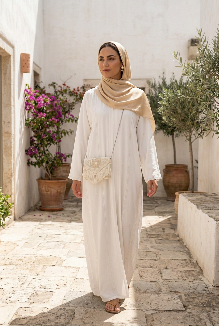 Ivory pearl sunburst fringe clutch worn crossbody on a silver chain with a white abaya and champagne shayla in a whitewashed courtyard
