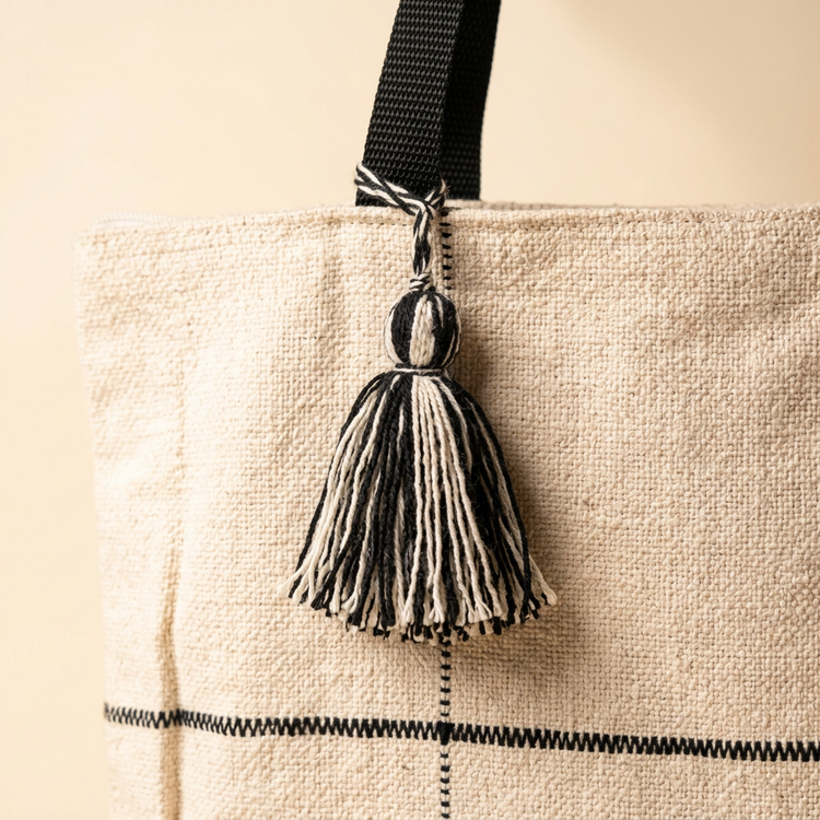 Close-up of woven cream fabric, black grid stitching and tassel detail