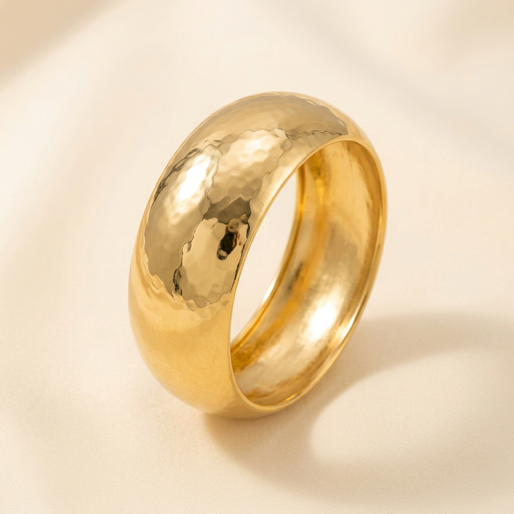 Wide hammered gold bangle on a cream background