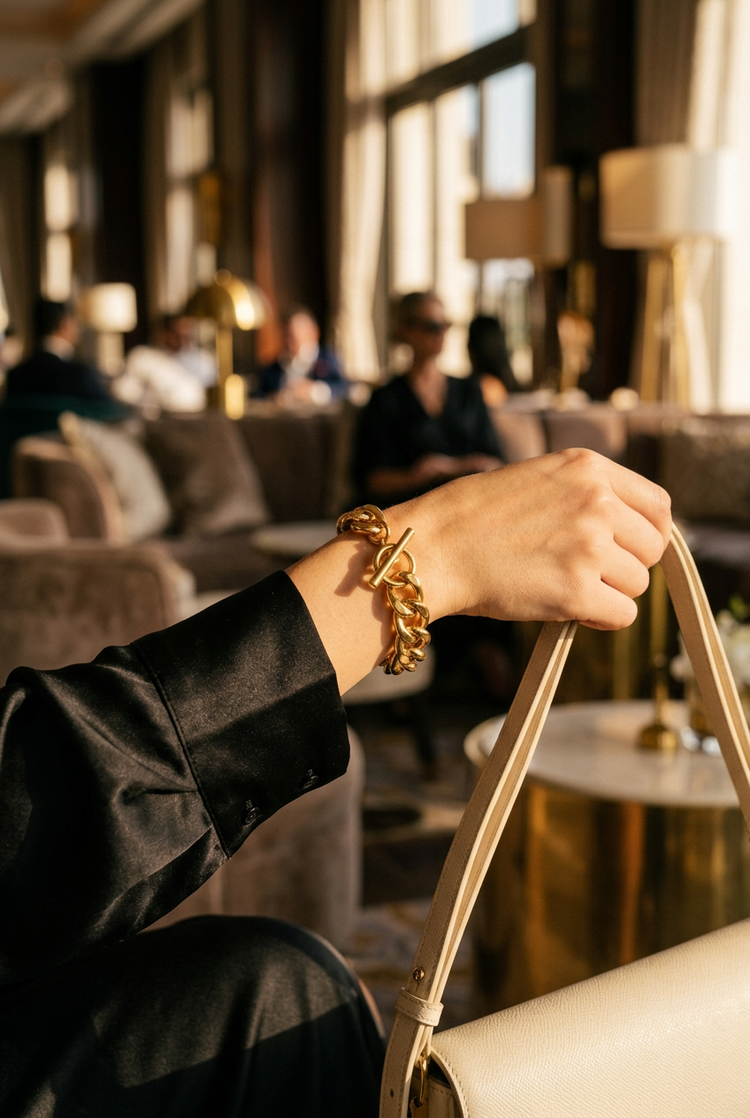 Woman holding a cream handbag wearing a chunky gold chain toggle bracelet