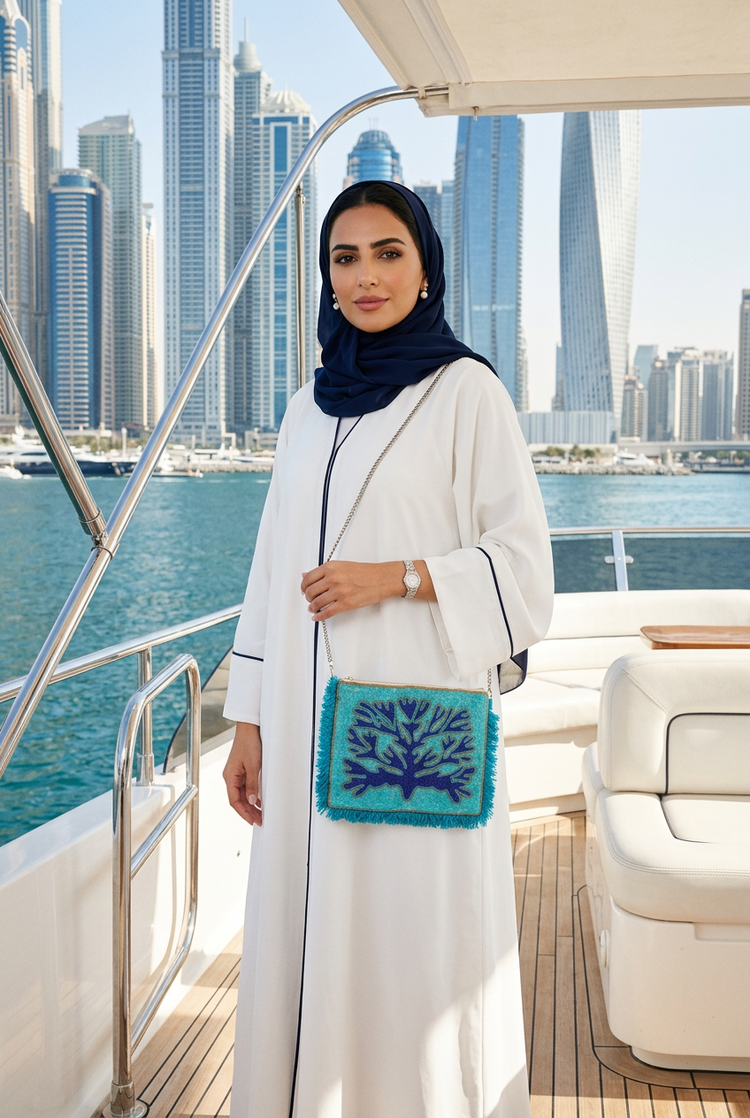 Turquoise and navy coral beaded fringe clutch on a silver chain with a navy-trimmed white abaya and navy shayla on a yacht at Dubai Harbour