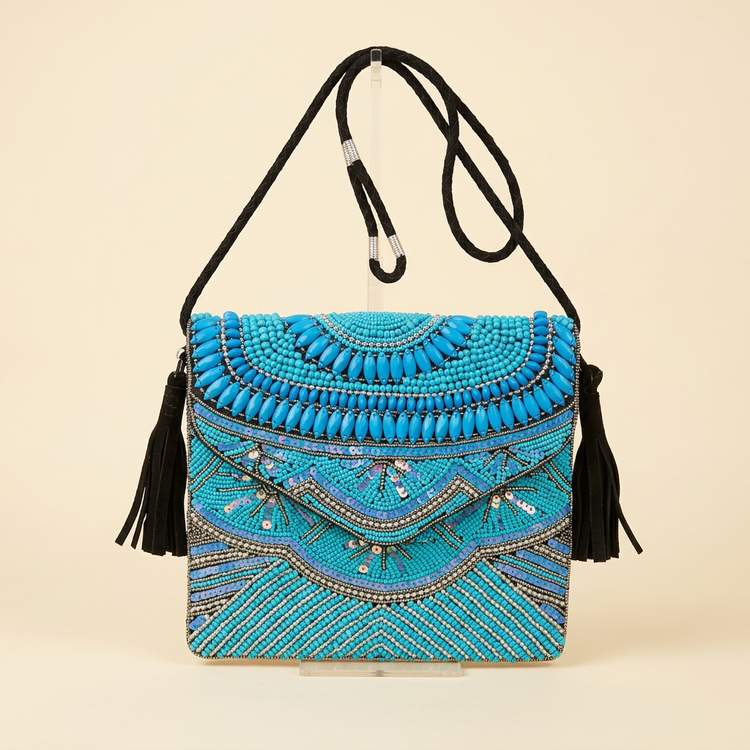 Turquoise beaded crossbody bag with black suede tassels on a cream studio background