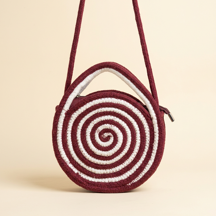 Round burgundy and white spiral rope crossbody bag on a cream studio background