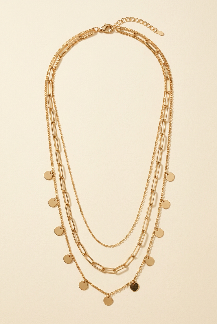 Layered gold coin chain necklace on a cream studio background