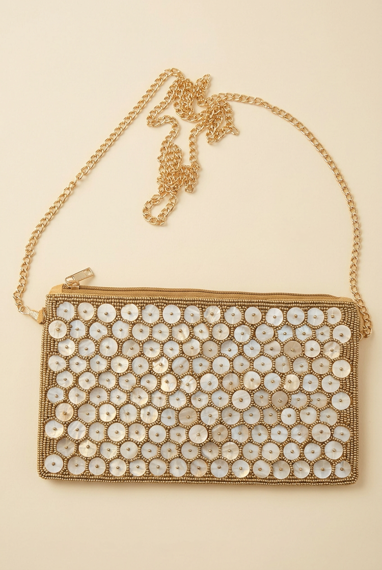Shell Glow shell-disc sling bag with zip top and long chain on an ivory studio background
