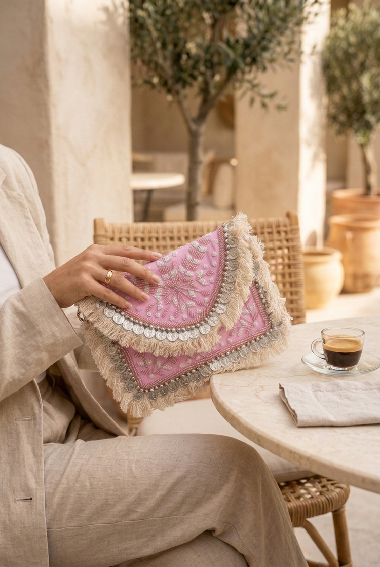 Close-up of the pink coin fringe boho clutch held with a beige linen outfit at an outdoor cafe
