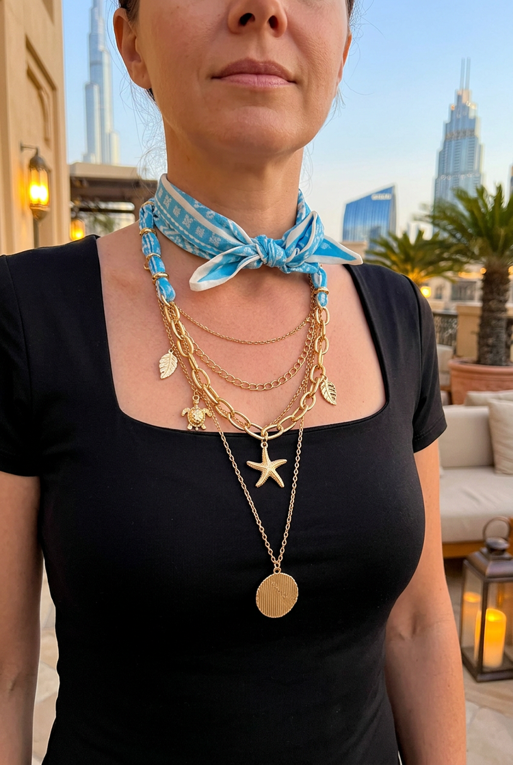 Blue scarf and gold seashell necklace worn with black in evening light