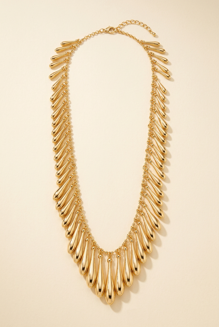 Gold teardrop fringe necklace on a cream studio background