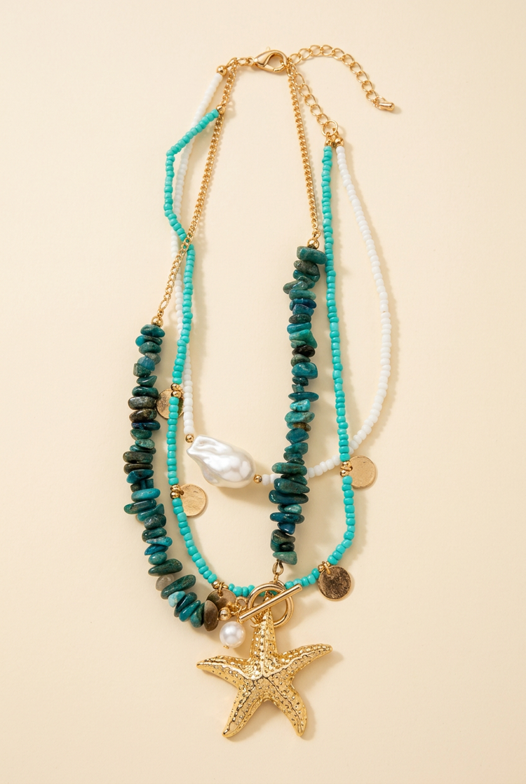 Layered turquoise beaded gold starfish necklace on a cream studio background