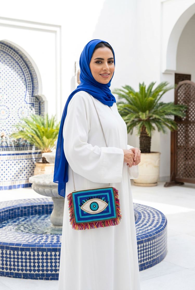 Blue and turquoise beaded eye fringe clutch on a silver chain with a white abaya and royal blue shayla in a tiled courtyard