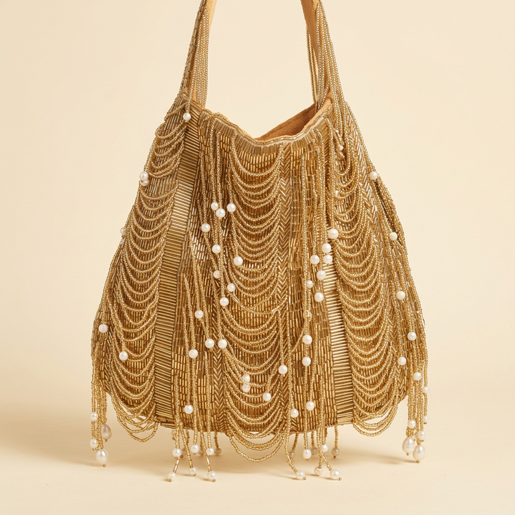 Gold beaded drawstring bag with pearl tassels on a cream studio background