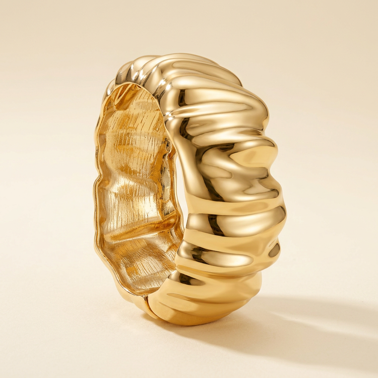 Sculpted ripple gold bangle on a cream studio background