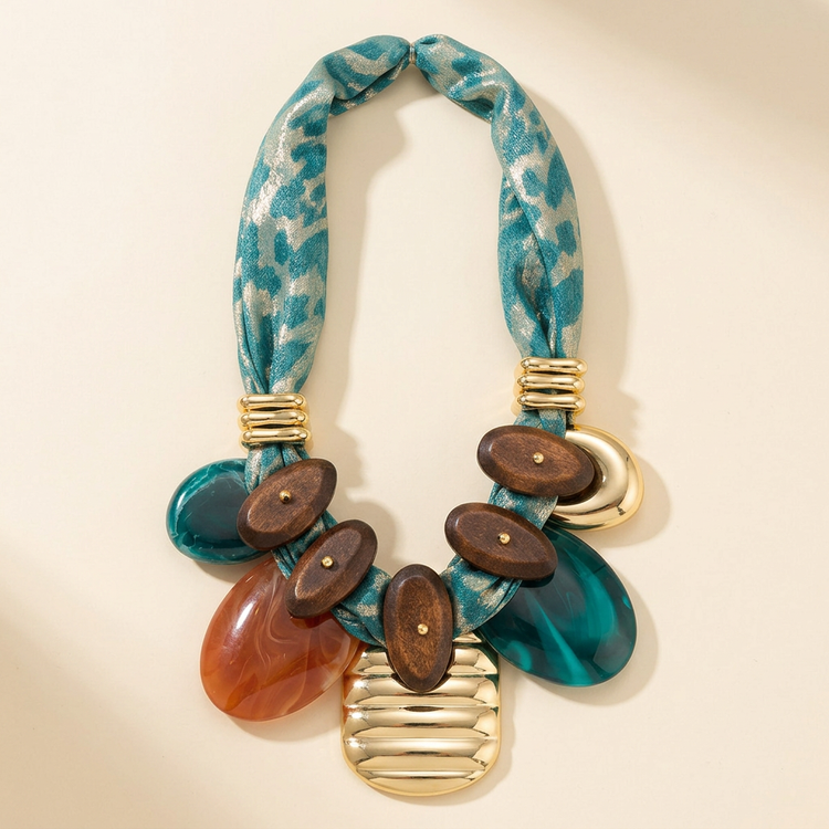 Teal scarf and sculpted gold charm necklace on cream studio background