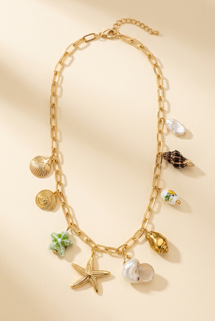 Gold paperclip sea charm necklace arranged on a cream studio background