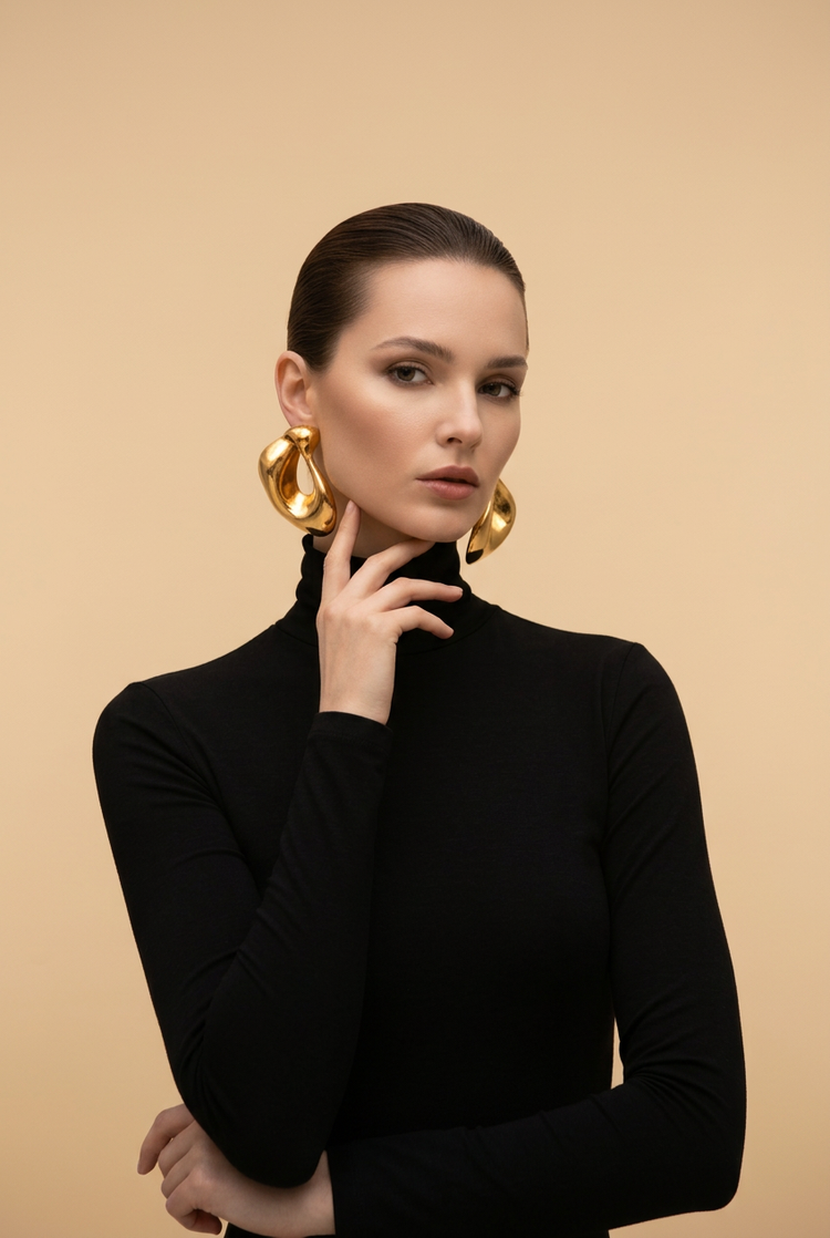 Model wearing oversized gold hoop earrings and a black turtleneck